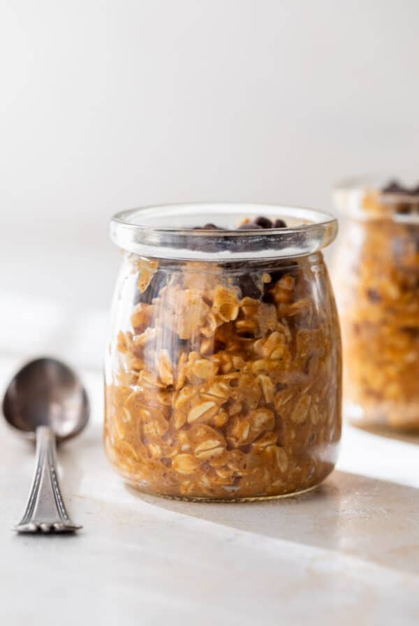 close up on pumpkin overnight oats in a glass jar next to a spoon.