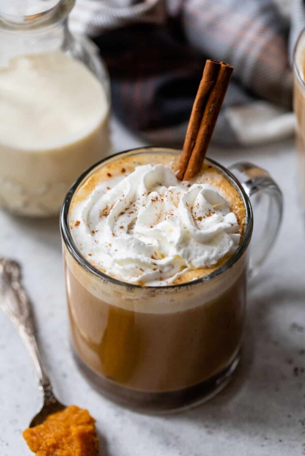 pumpkin spice latte in a glass with whipped cream and a cinnamon stick