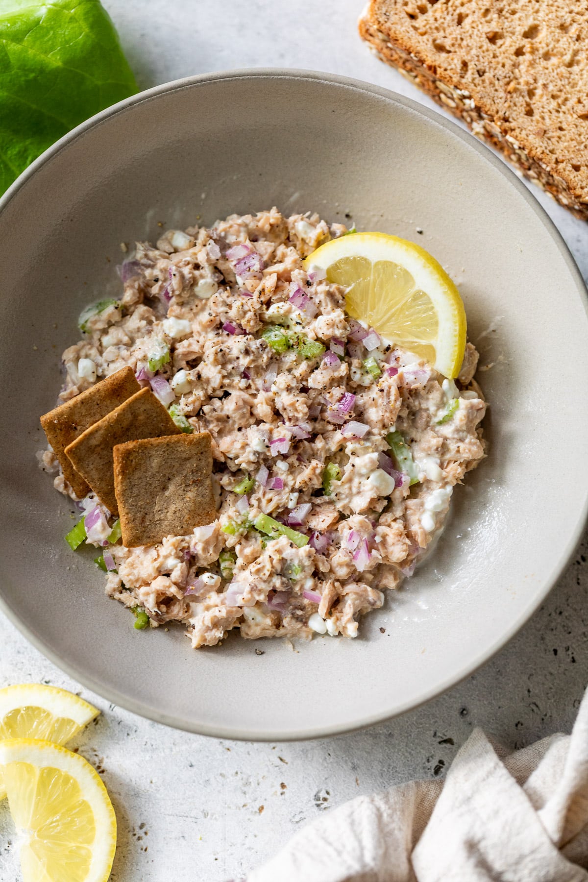 a bowl of salmon salad topped with a lemon wedges and crackers.