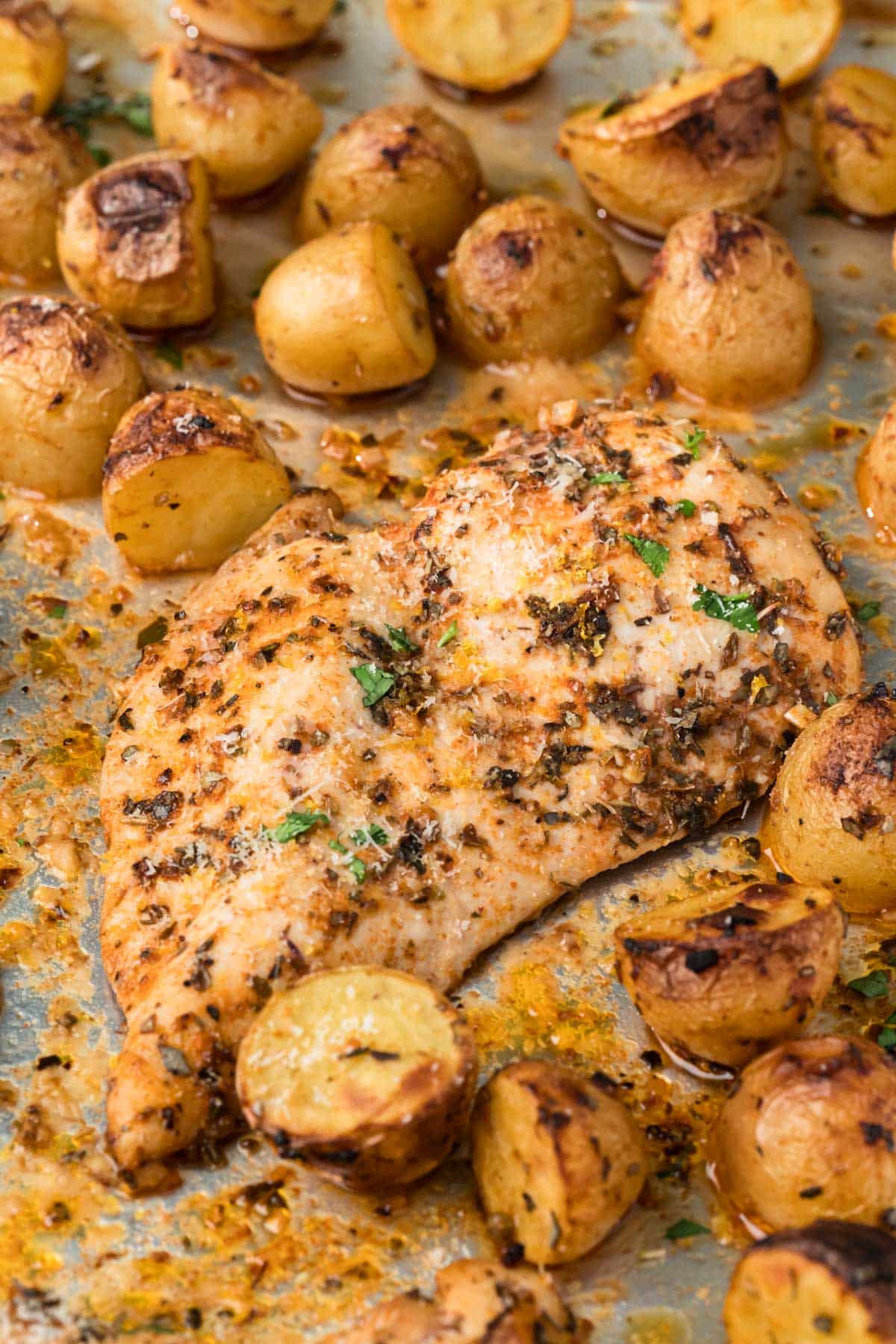 Close up on a roasted chicken breast surrounded by roasted potatoes on a sheet pan.