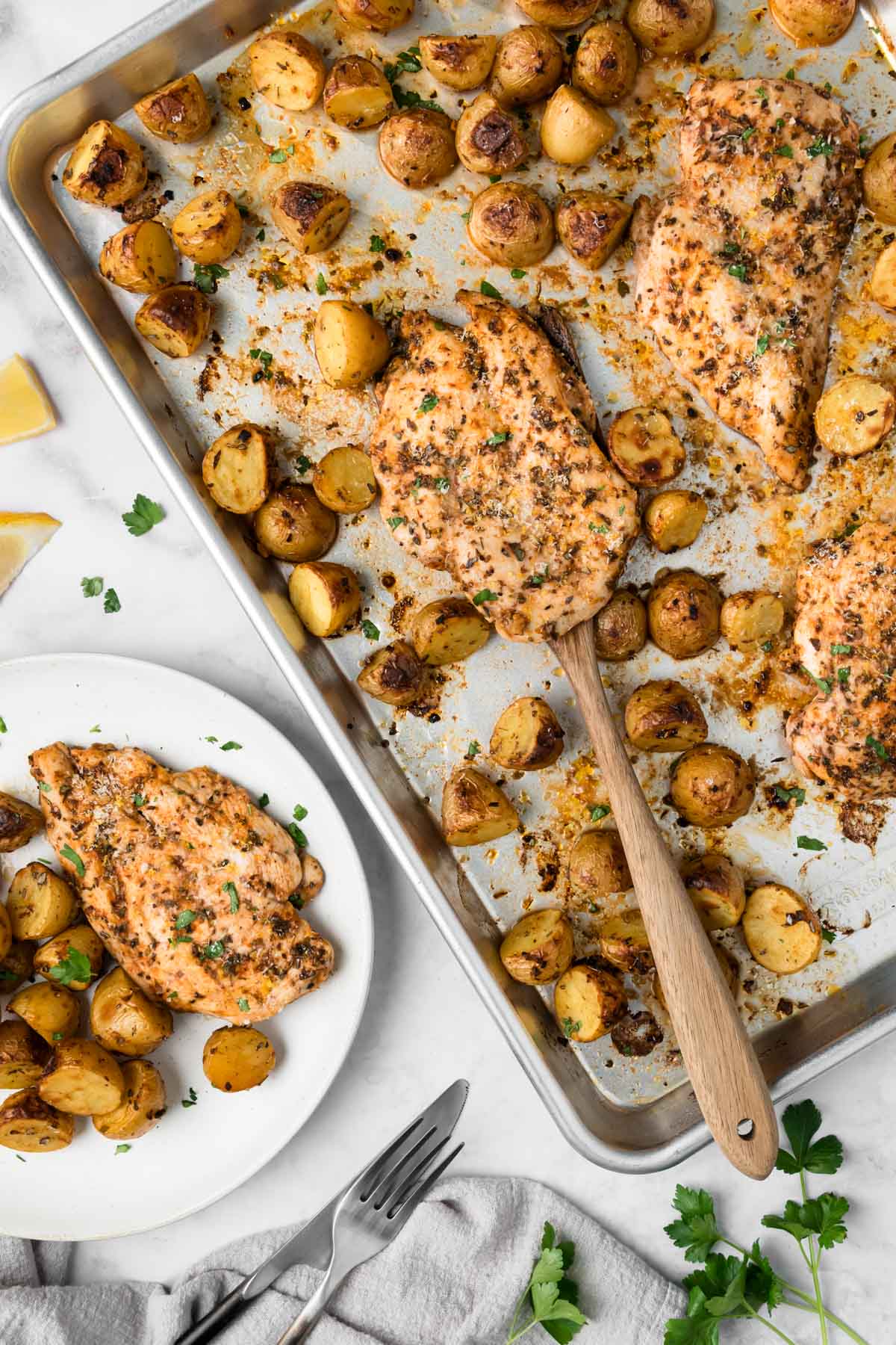 Overhead view of roasted chicken and potatoes on a sheet pan next to a plate of chicken and potatoes.