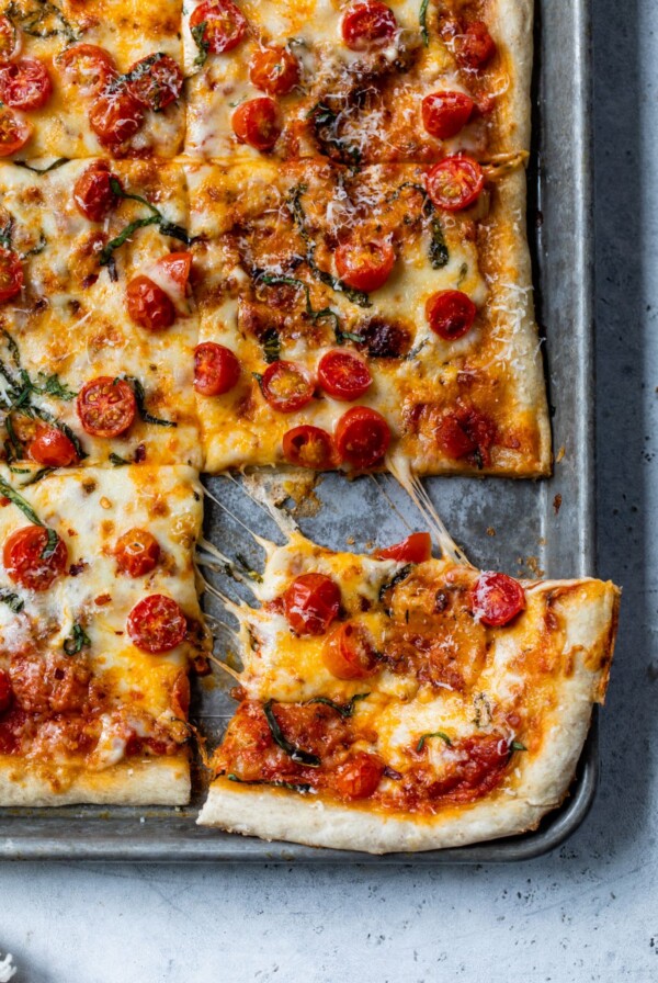 a slice of pizza being pulled away from the rest of the pizza on a baking sheet