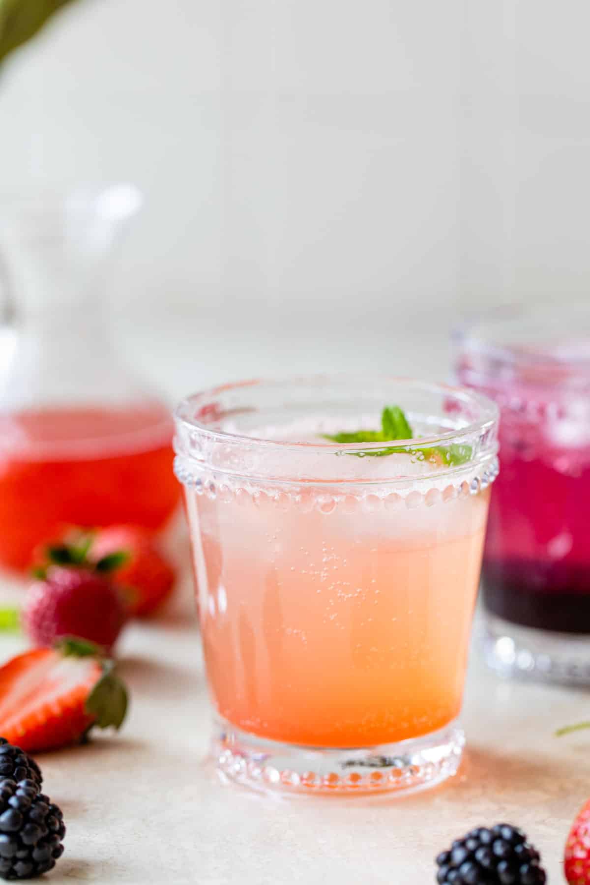 two cocktail glasses with fruity drinks in them besides fresh strawberries and fresh blackberries