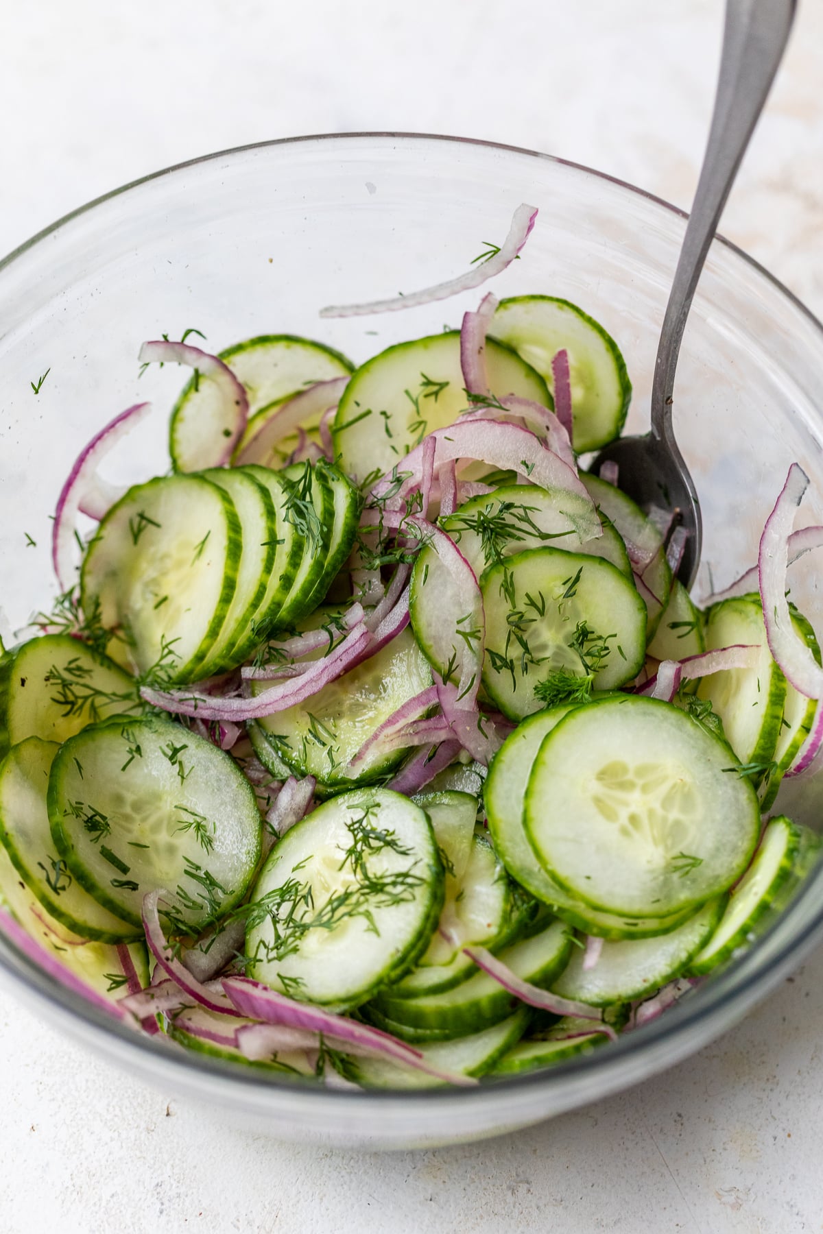 tossing cucumbers, onions, and dill together in a glass bowl for a simple cucumber salad.