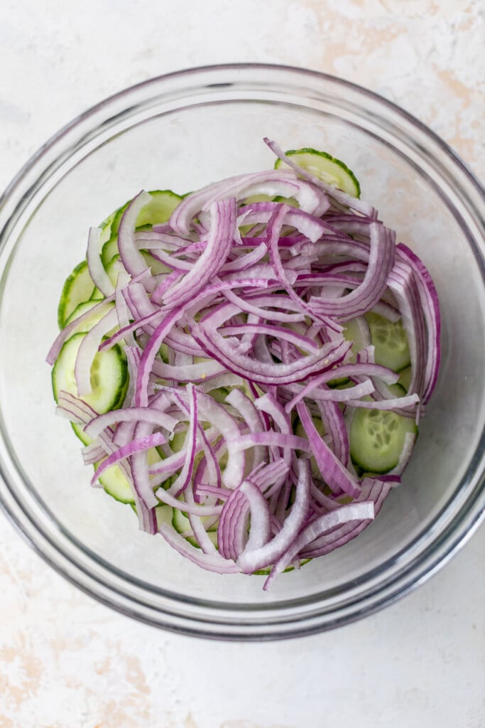 sliced red onions and sliced cucumbers in a large glass bowl.