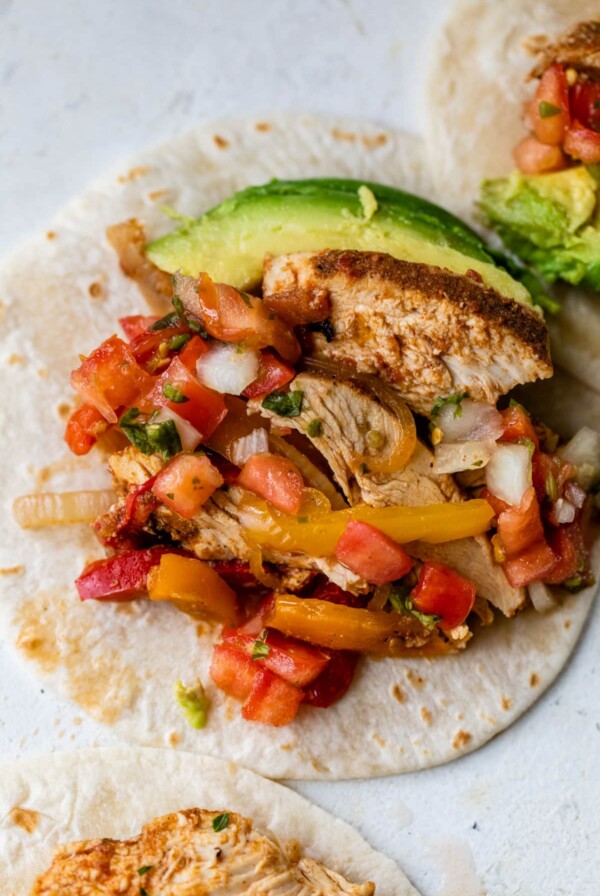 slow cooker chicken fajitas on top of a tortilla and top with sliced avocado