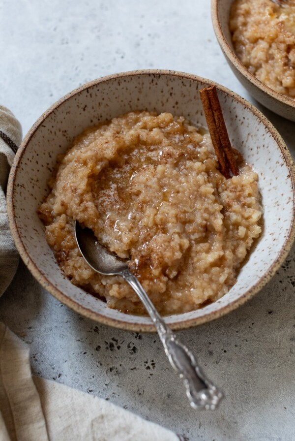 slow cooker rice pudding in a bowl with a spoon and a cinnamon stick