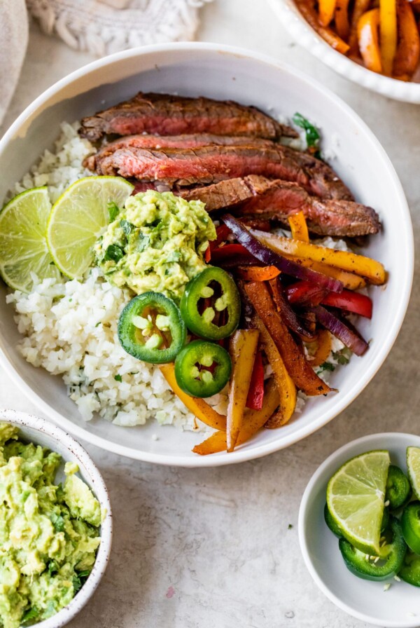a bowl filled with cauliflower rice, steak, peppers, and guacamole