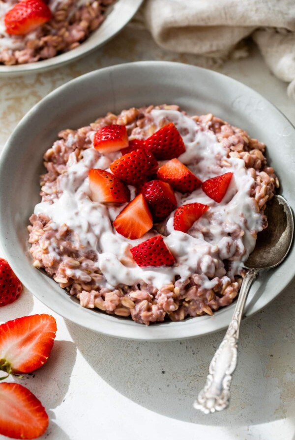 a bowl of pink-colored oats topped with yogurt and chopped strawberries