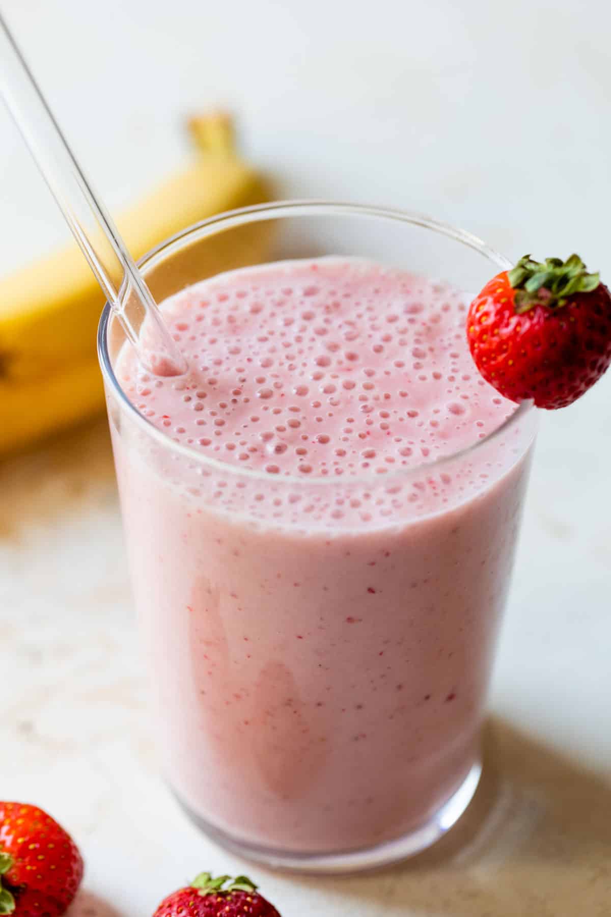 strawberry banana smoothie in a glass with a straw and strawberry on the edge of the glass