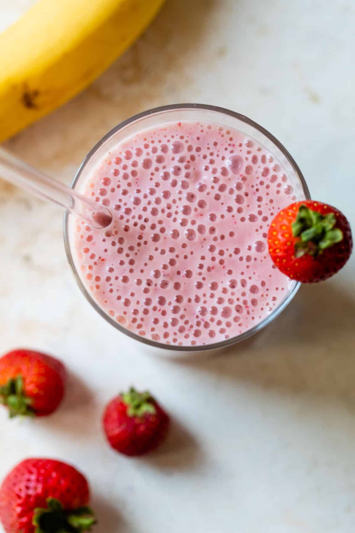 overview of a strawberry banana smoothie in a glass with a straw and strawberry on the edge of the glass