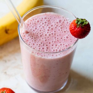 strawberry banana smoothie in a glass with a straw and strawberry on the edge of the glass