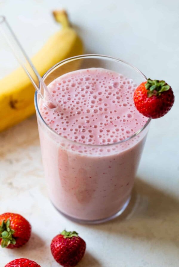 strawberry banana smoothie in a glass with a straw and strawberry on the edge of the glass