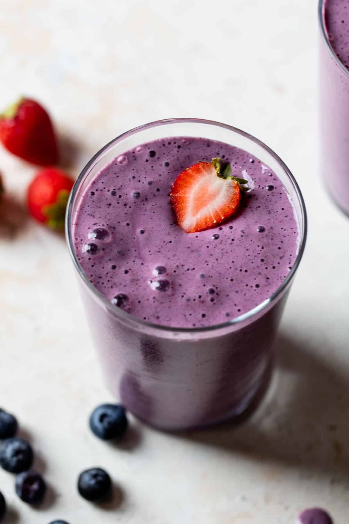 strawberry blueberry smoothie in a glass with sliced strawberry on top