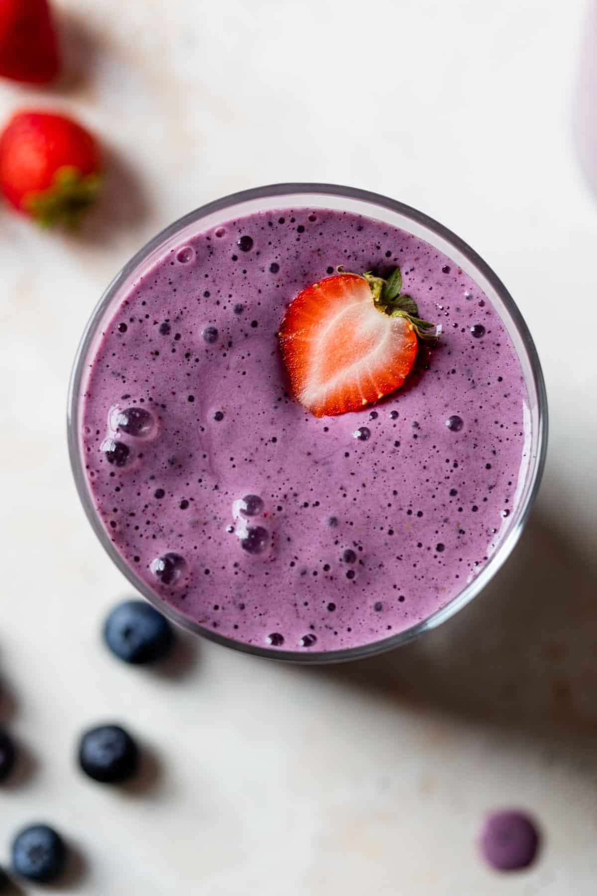 overview of strawberry blueberry smoothie in a glass with sliced strawberry on top