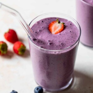 strawberry blueberry smoothie in a glass with a straw and sliced strawberry on top
