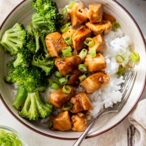 teriyaki chicken and broccoli served over white rice in a bowl.