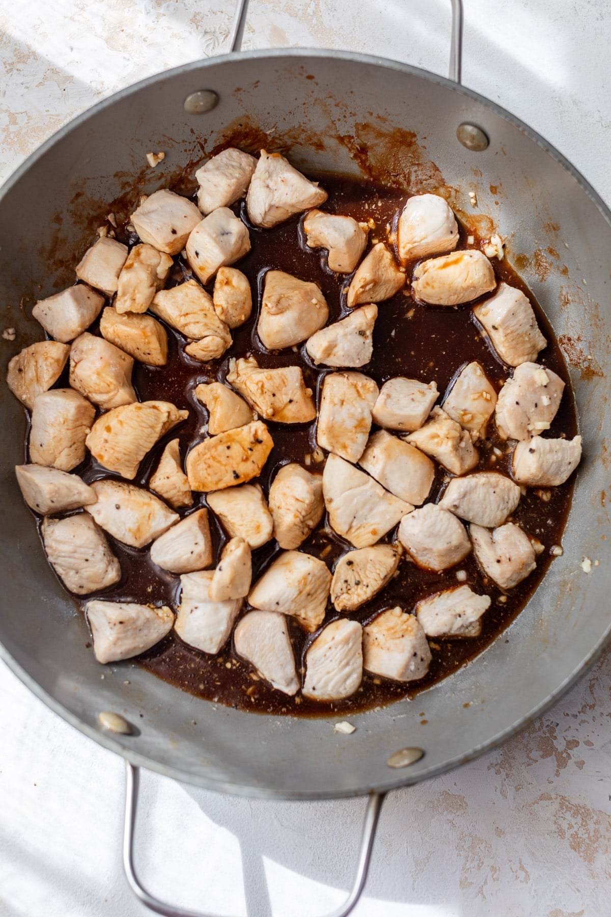 overhead view of cooked chicken bites covered in teriyaki sauce in a large skillet.