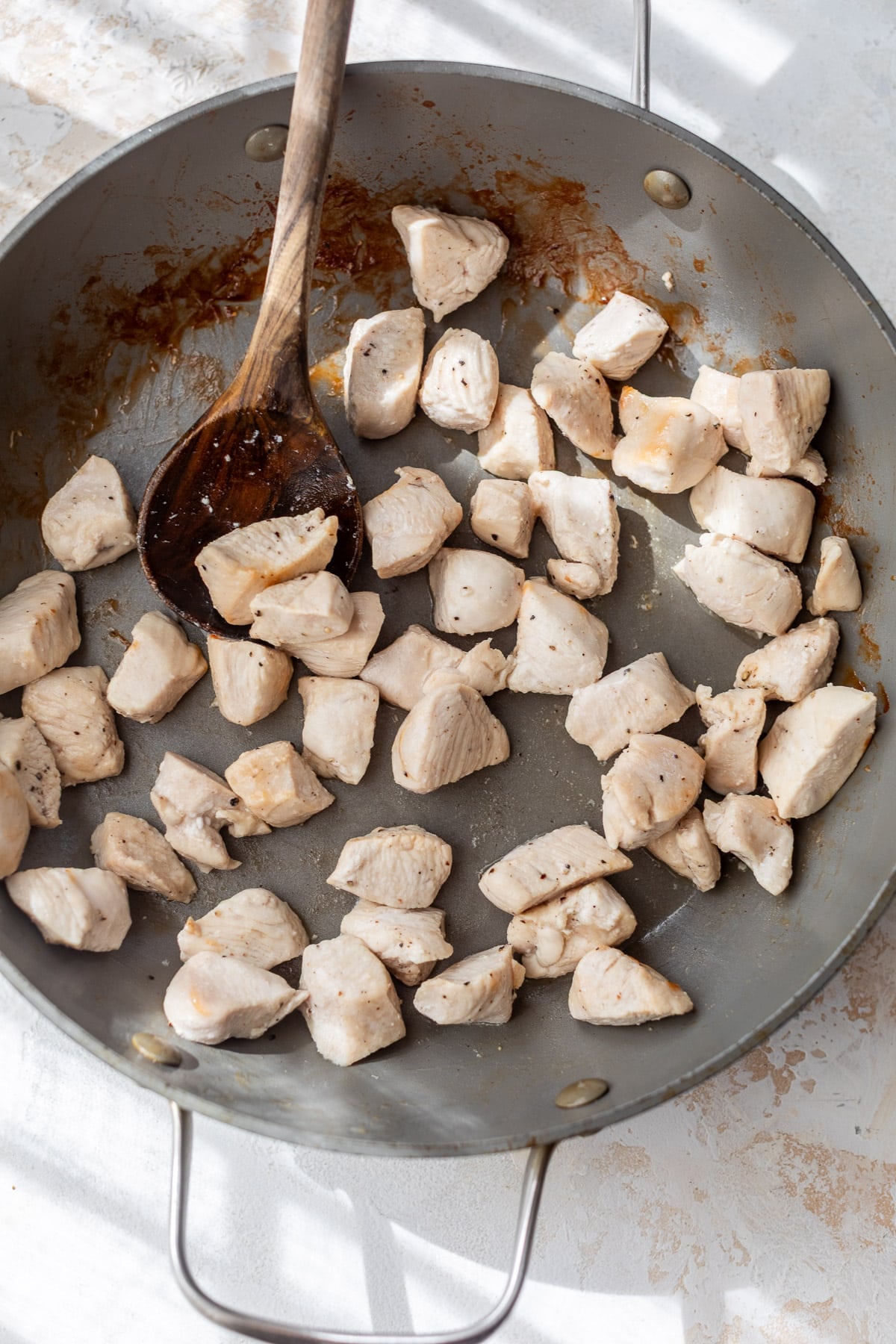using a wooden spoon to stir cooked chicken bites in a large skillet.