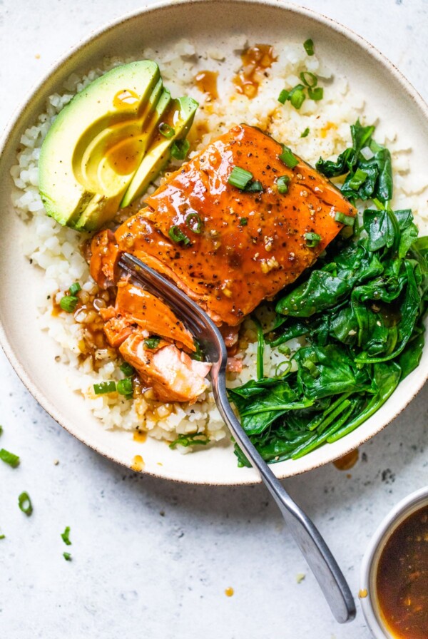 a bowl filled with cauliflower rice, salmon, cooked spinach, and avocado slices