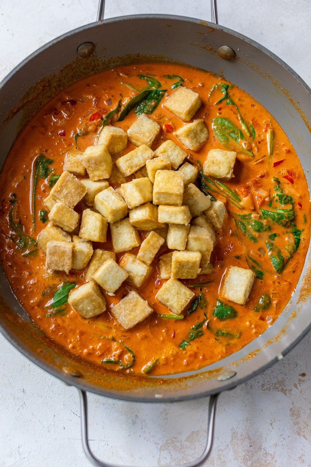 a pile of crispy golden brown tofu cubes in a red curry sauce in a large grey skillet.