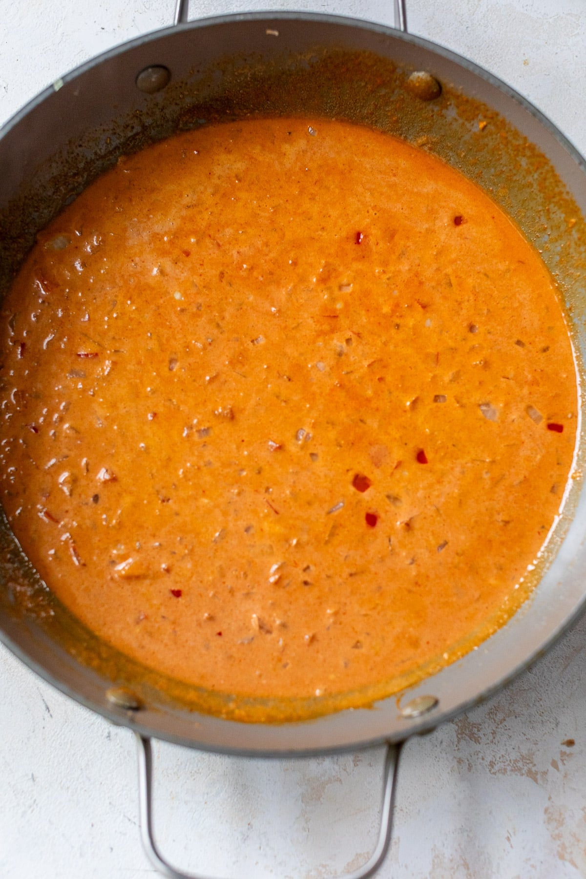 a red curry sauce cooking in a large grey skillet.