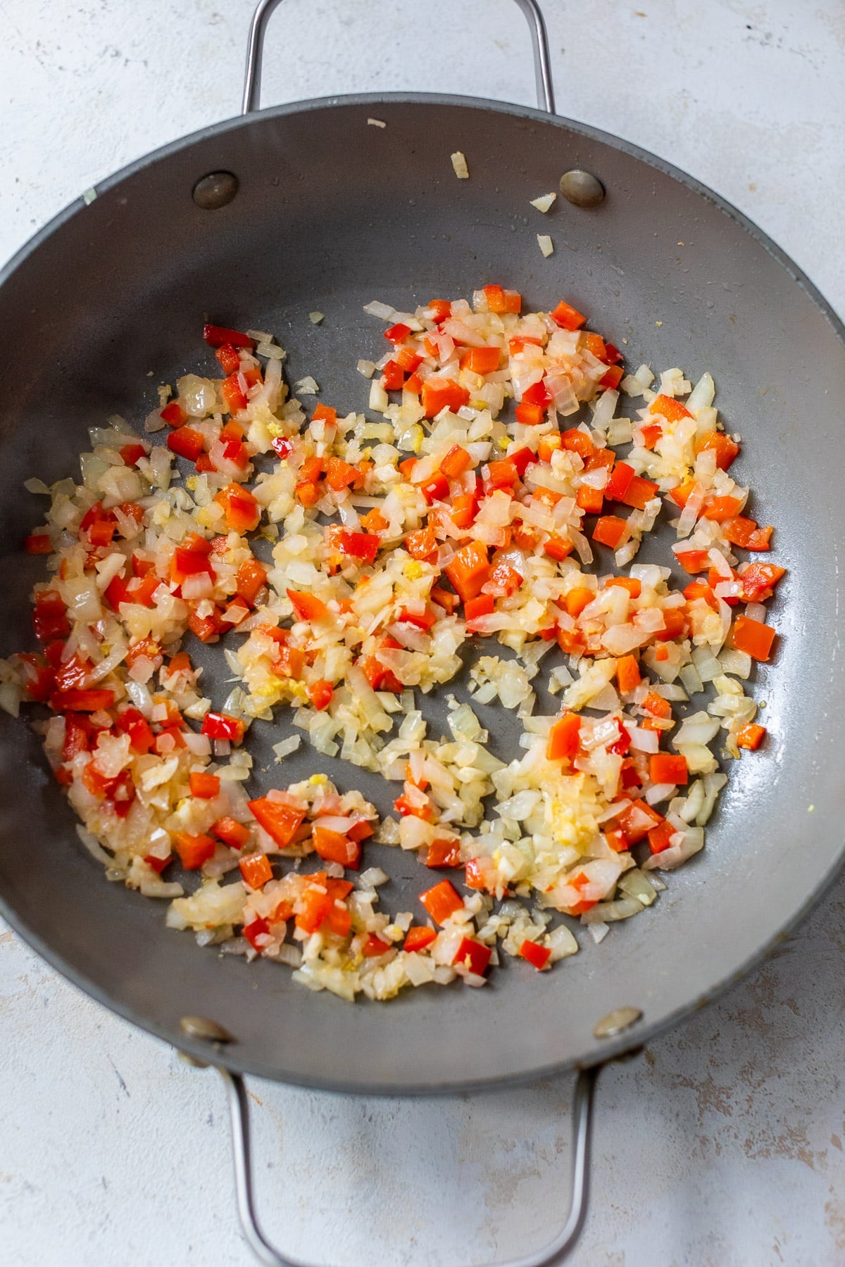 cooking diced onions, red peppers, and garlic in a large grey skillet.