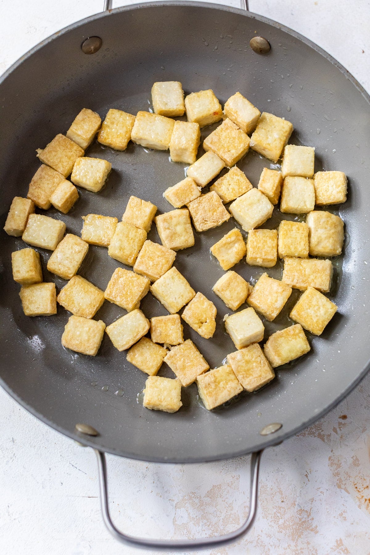frying golden tofu cubes in a large grey skillet.