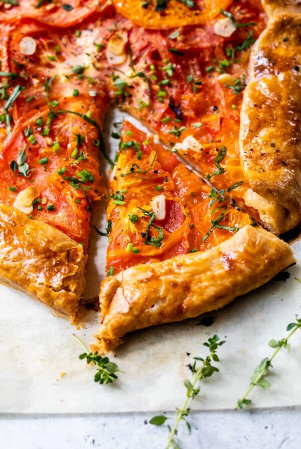 close-up of tomato galette with fresh thyme and chives on top and a slice cut out