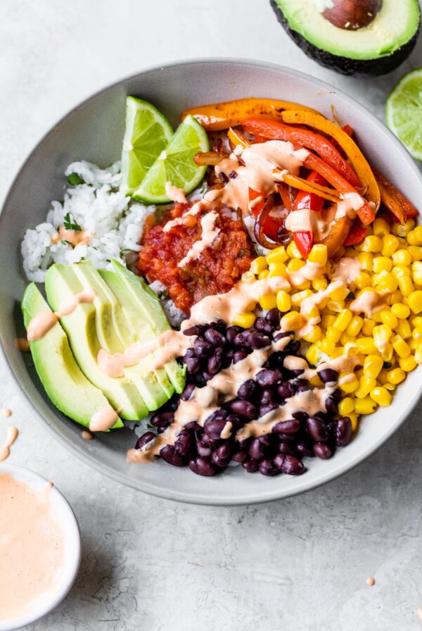 bowl of rice topped with black beans, corn, peppers, avocado, salsa, and chipotle aioli