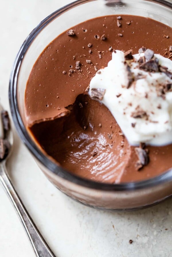 a close-up of a bowl of vegan chocolate pudding with whipped cream on top and chopped chocolate