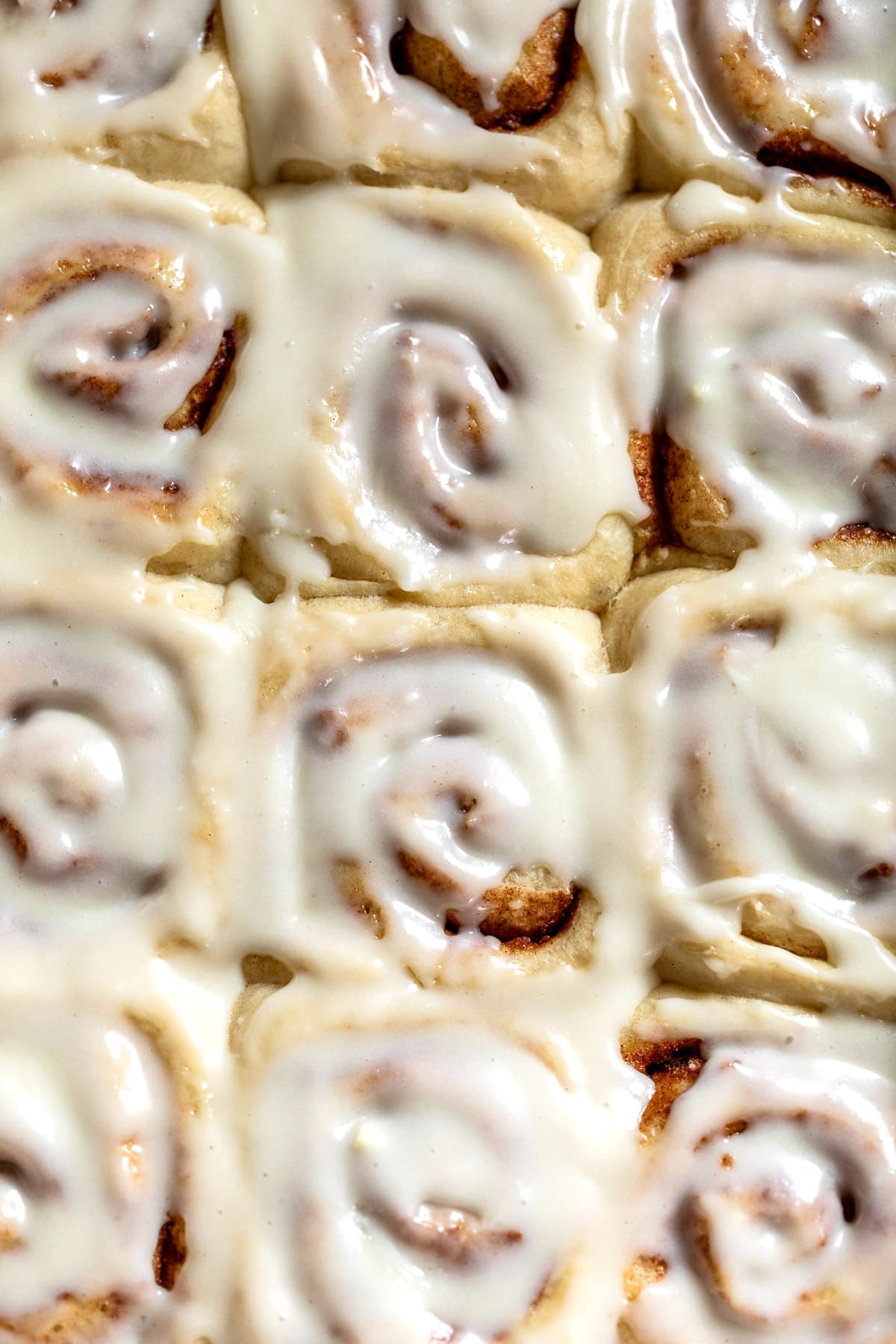 close up on cream cheese frosting-topped vegan cinnamon rolls in a white baking dish.