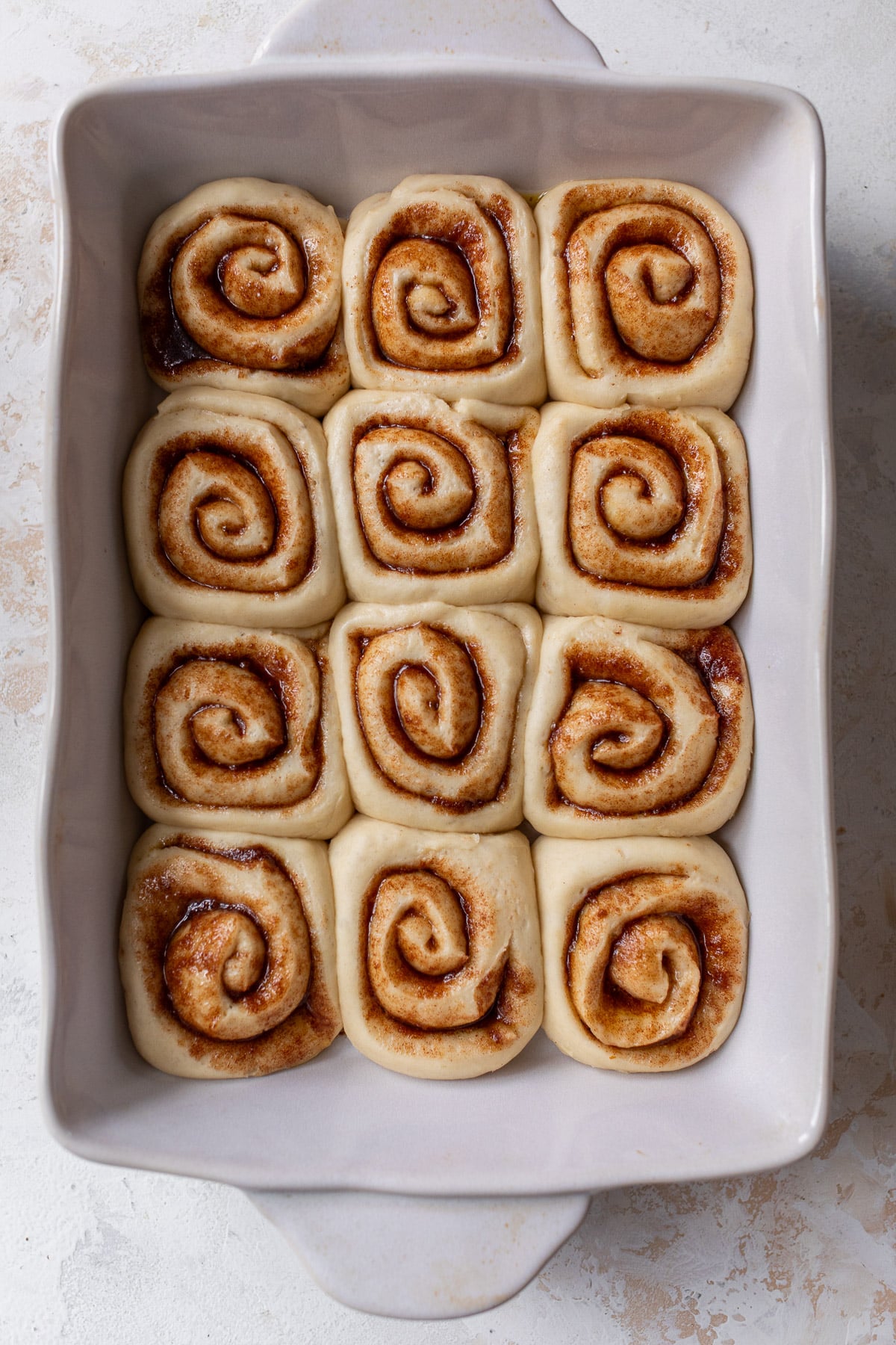 overhead view of risen and unbaked vegan cinnamon rolls in a white baking dish.