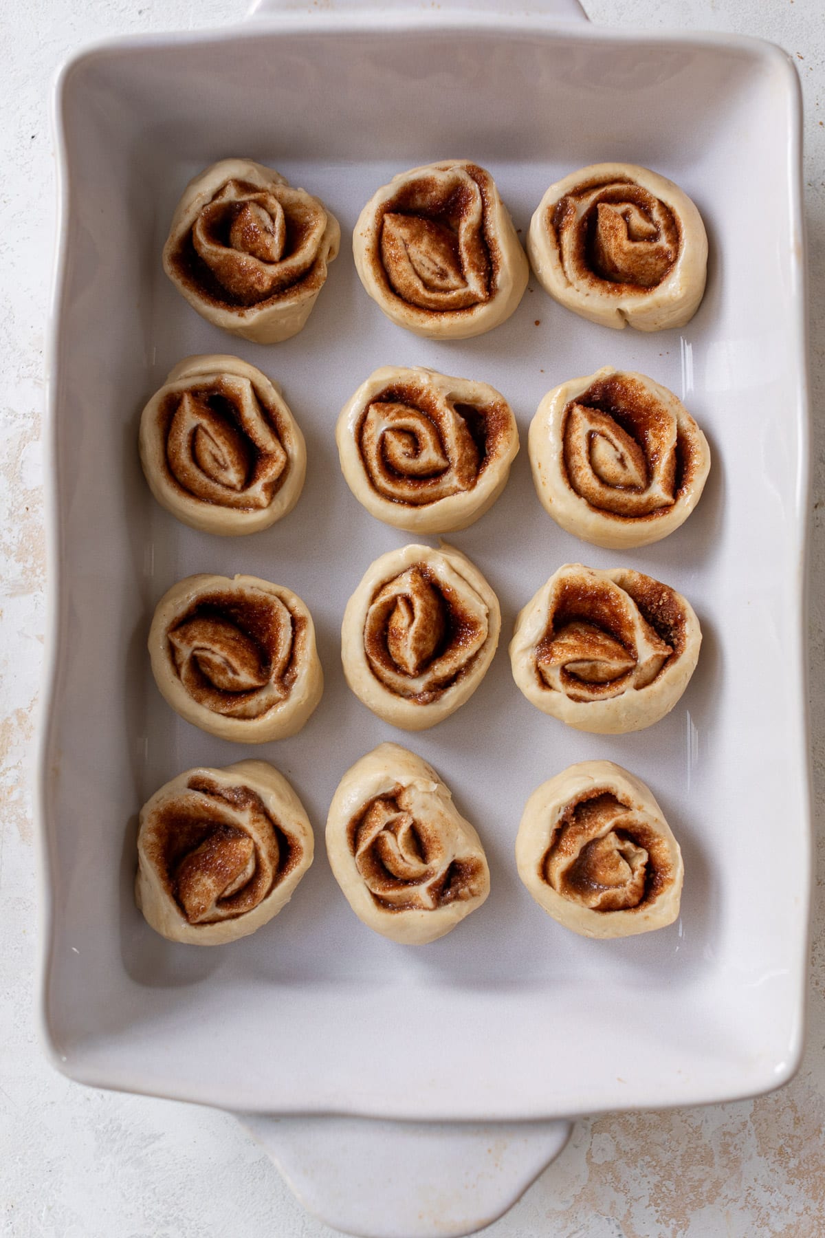 overhead view of unbaked vegan cinnamon rolls in a white baking dish.