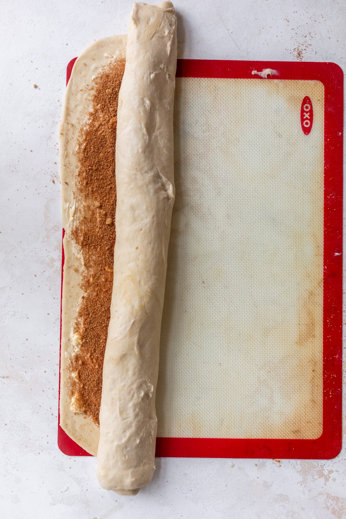 overhead view of a half-rolled log of vegan cinnamon roll dough on a baking mat.
