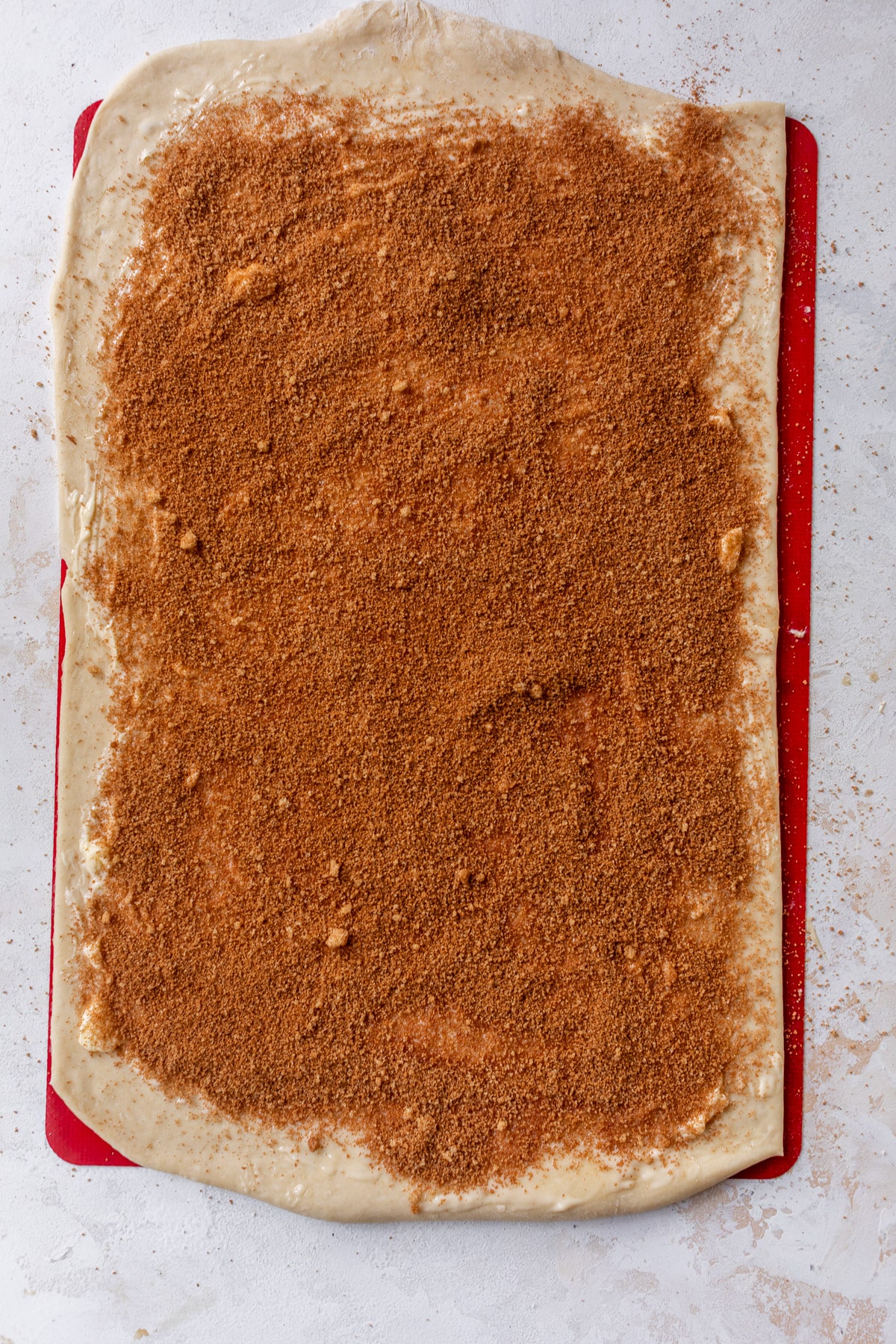 overhead view of a rectangle of vegan cinnamon roll dough topped with a layer of cinnamon sugar.