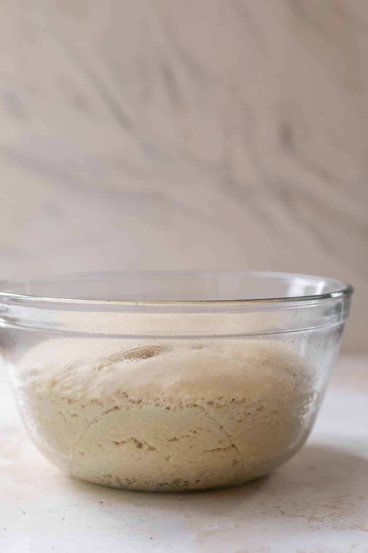 side view of risen vegan cinnamon roll dough in a glass bowl.