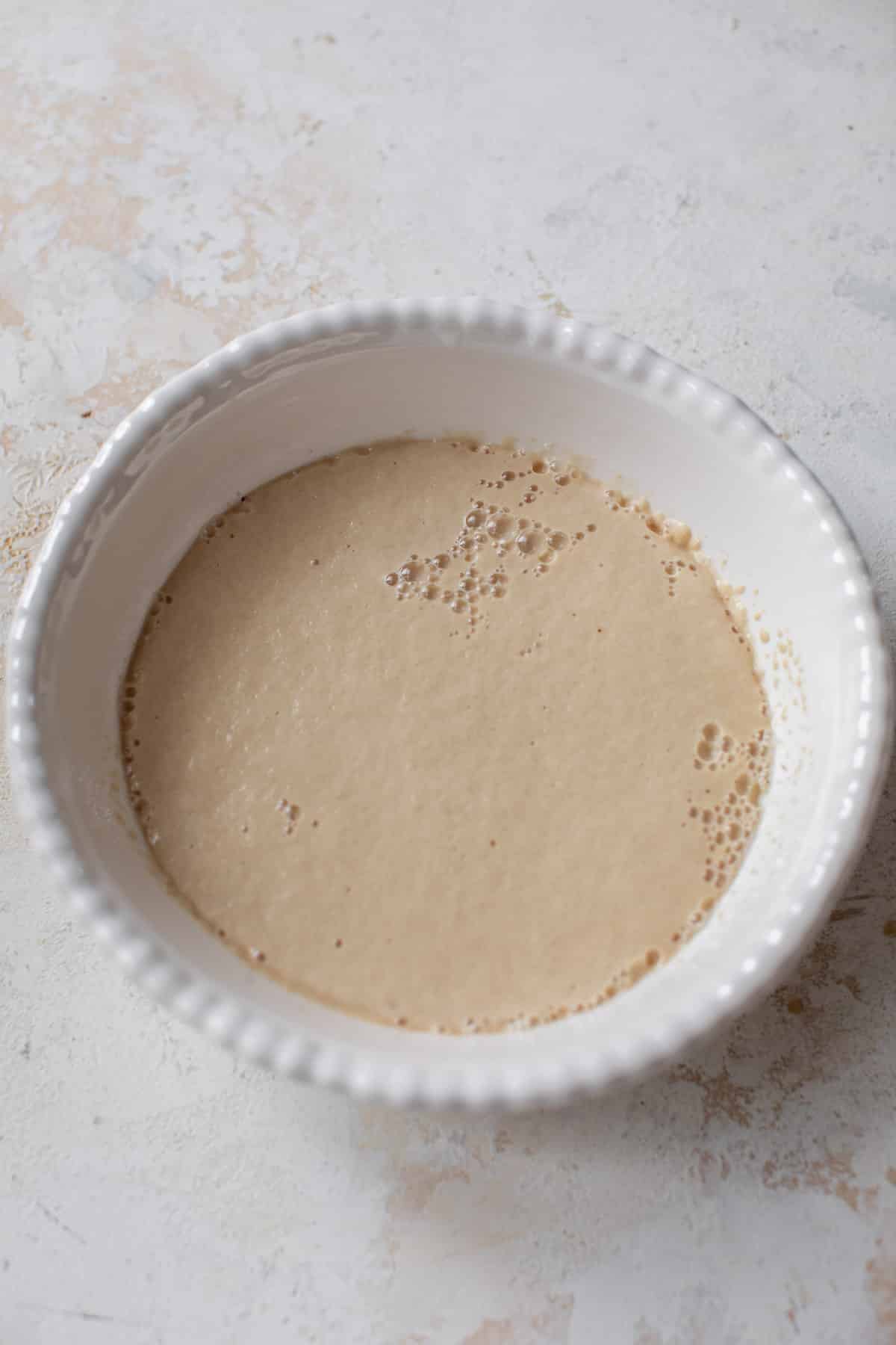 overhead view of a bubbly yeast mixture for vegan cinnamon rolls in a white bowl.