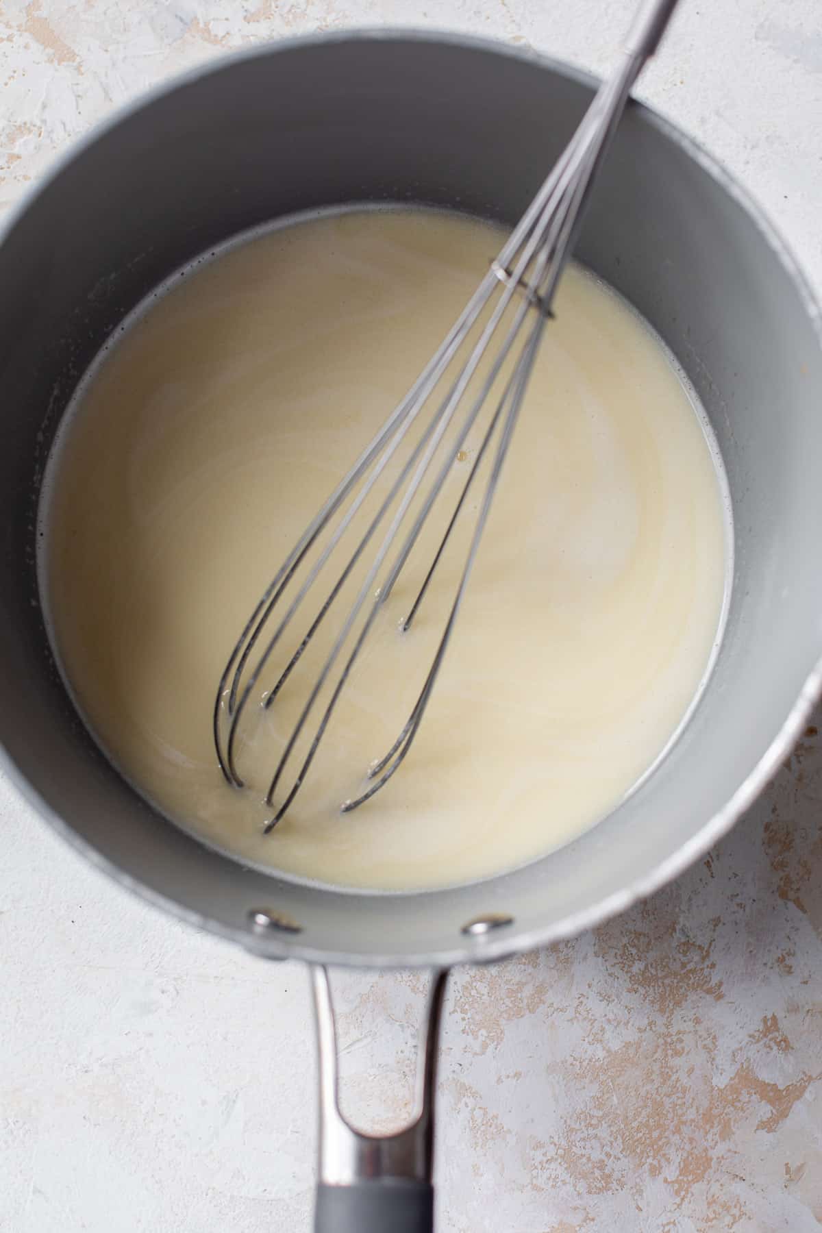 overhead view of a whisk in a liquid butter-milk mixture for vegan cinnamon rolls in a saucepan.