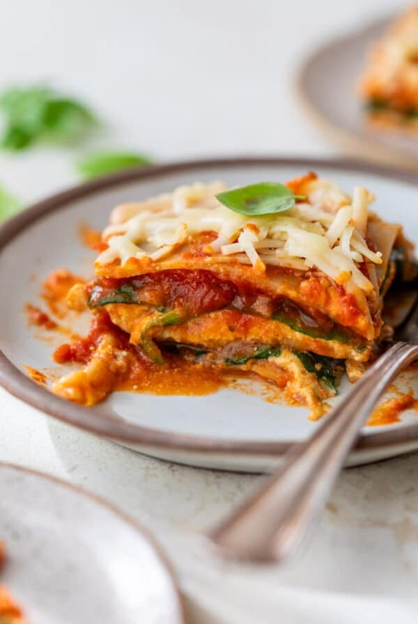 side view of a slice of vegan lasagna on a plate with a fork on the side.