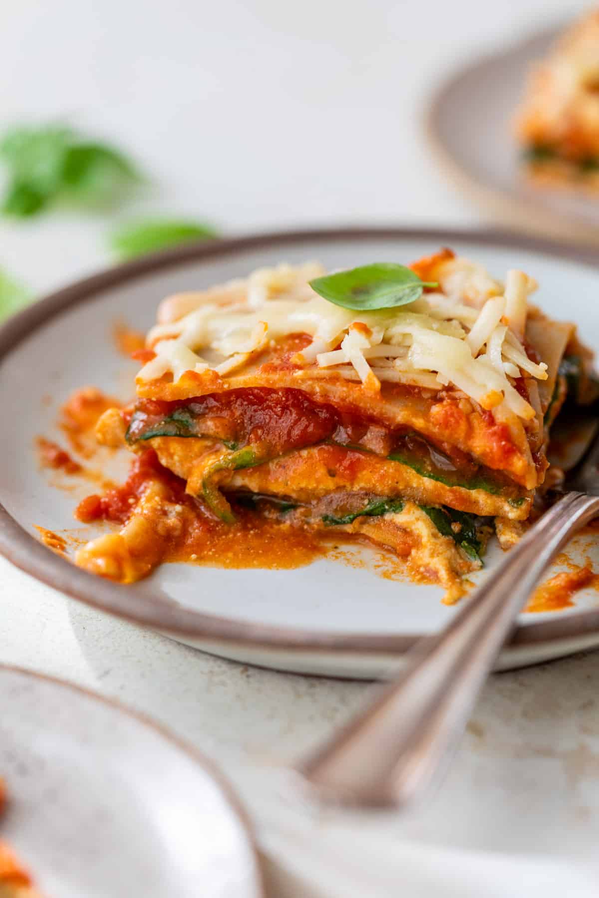 side view of a slice of vegan lasagna on a plate with a fork on the side.