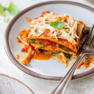 side view of a slice of vegan lasagna on a plate with a fork on the side.