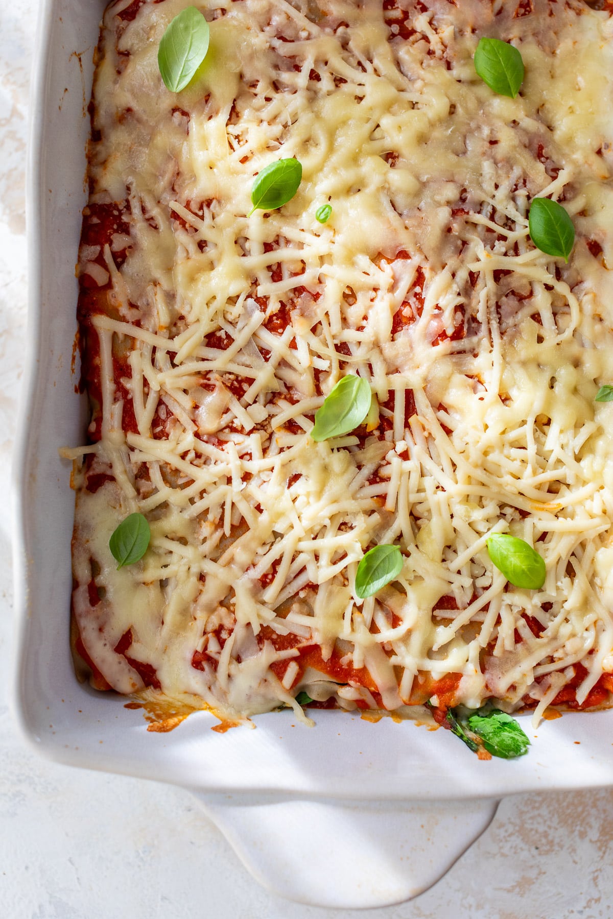 overhead view of a baked vegan lasagna topped with vegan mozzarella in a white baking dish.