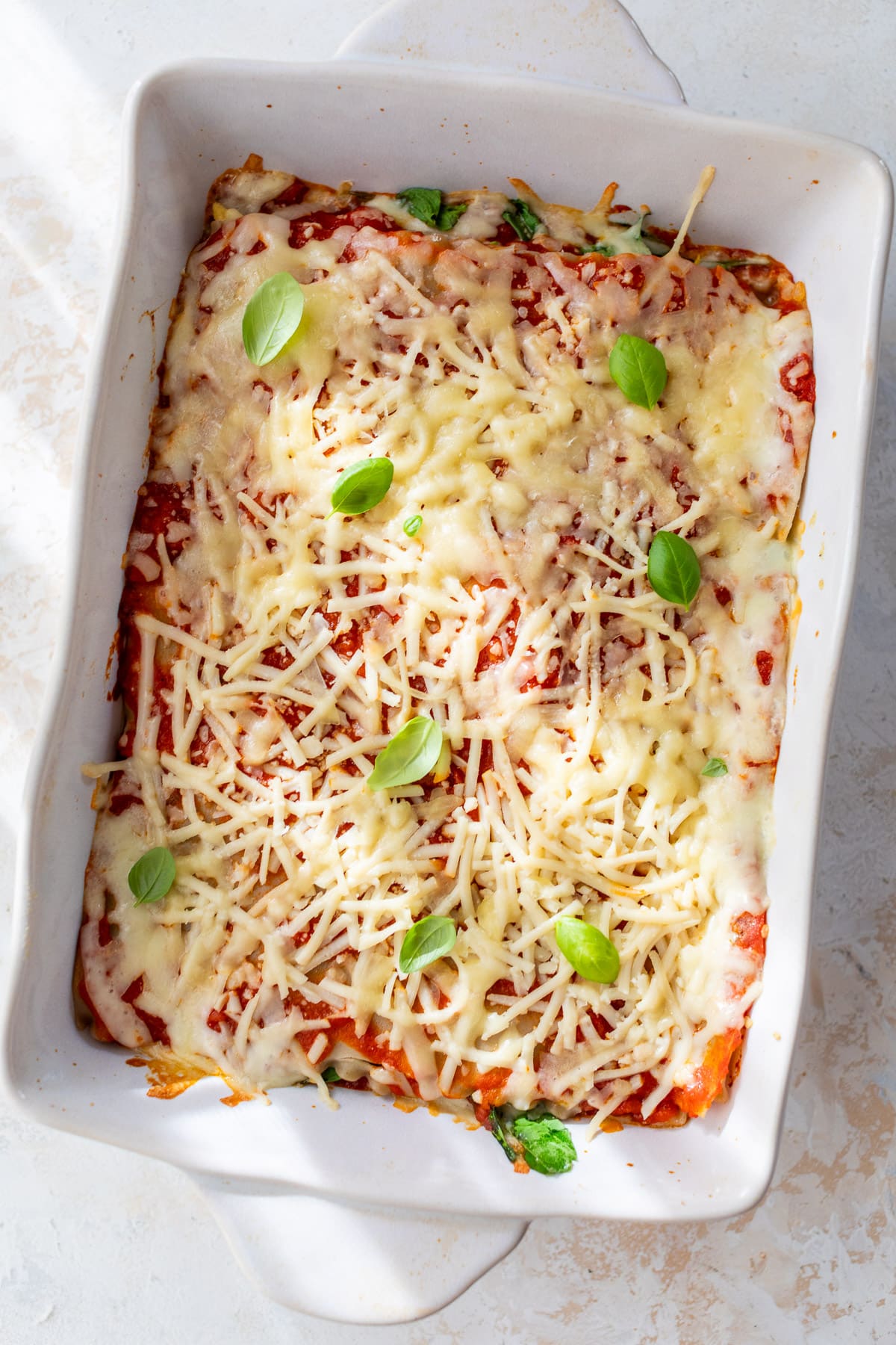 overhead view of a baked vegan lasagna topped with vegan mozzarella in a white baking dish.