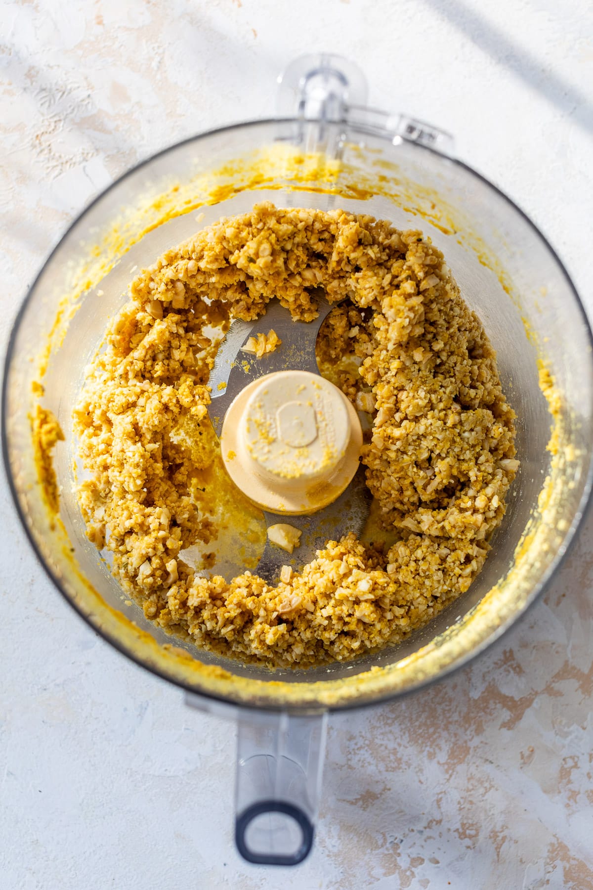 overhead view of a crumbly vegan ricotta cheese for vegan lasagna in a food processor.