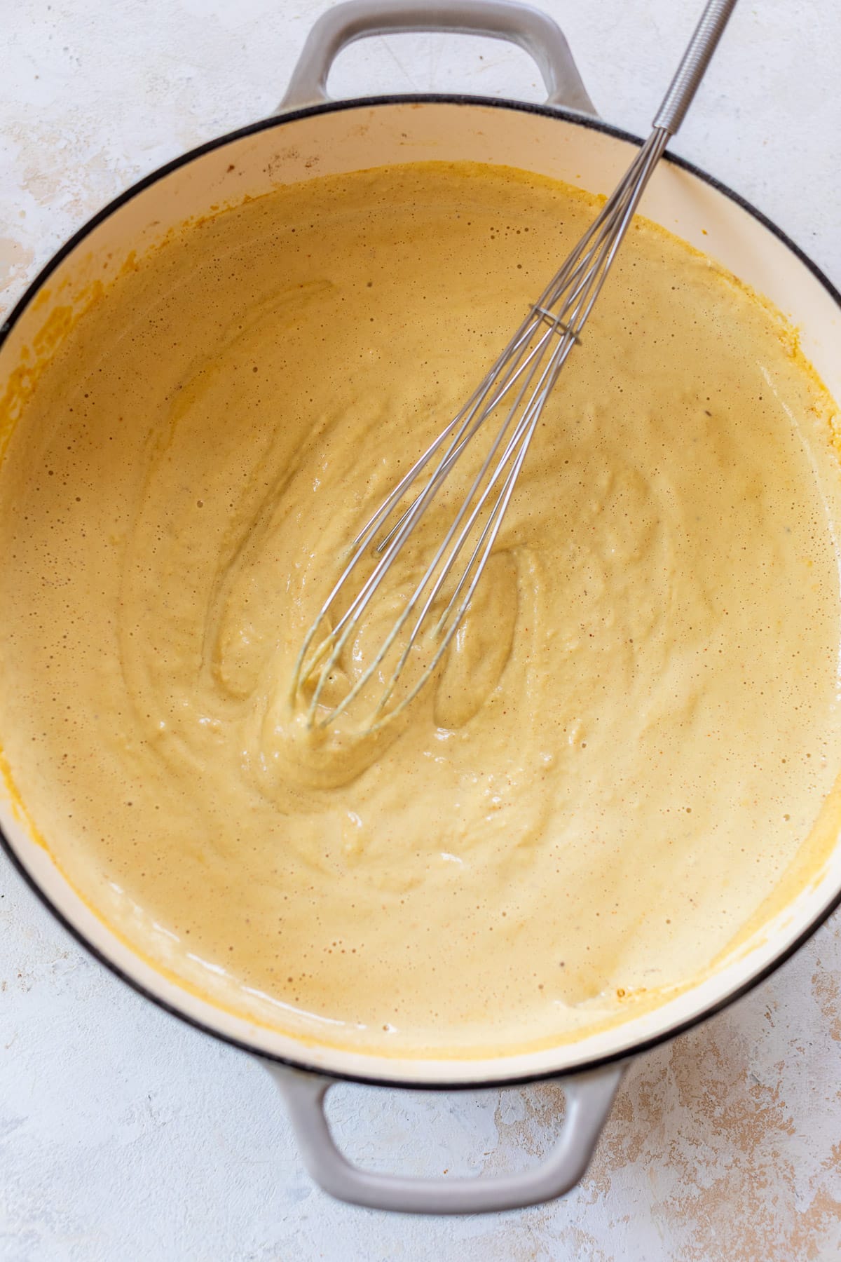 overhead view of a whisk in a pot of orange vegan mac and cheese sauce.