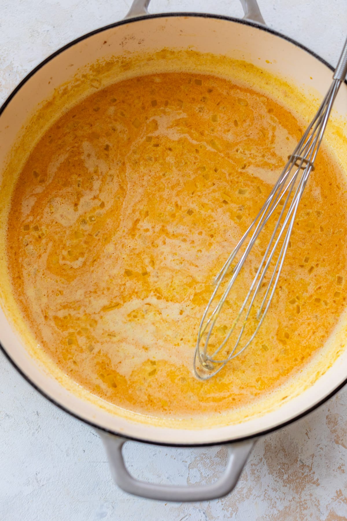 overhead view of a whisk in a pot of cheese sauce for vegan mac and cheese.