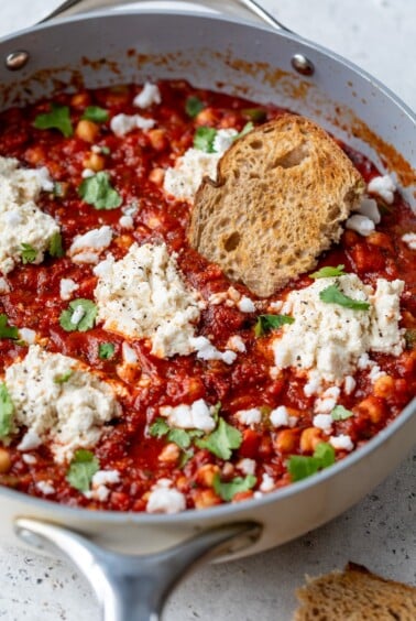 vegan shakshuka in a skillet with dollops of vegan ricotta and a slice of bread