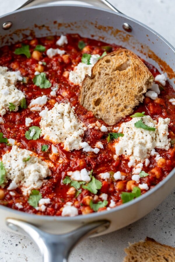 vegan shakshuka in a skillet with dollops of vegan ricotta and a slice of bread