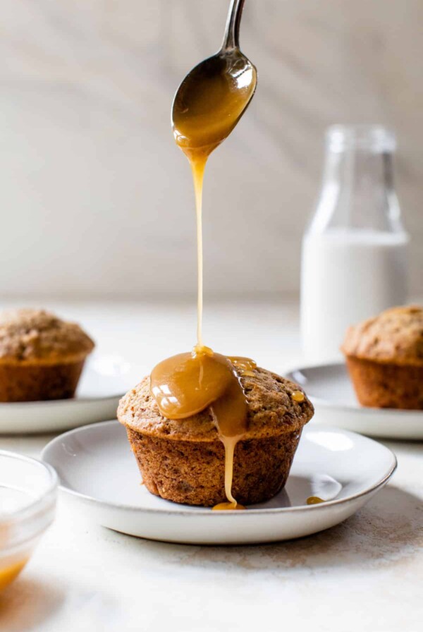 a vegan sticky toffee pudding on a plate with caramel drizzled over the top with a spoon